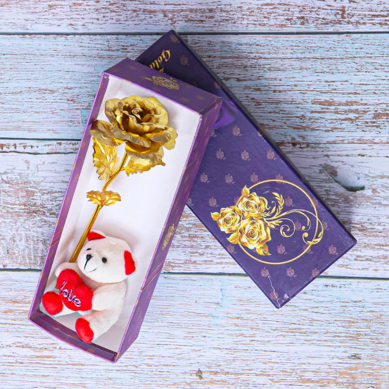 Teddy Embraced Rose gift set featuring a small white teddy bear with red accents holding a heart and a gold rose in a purple floral gift box.