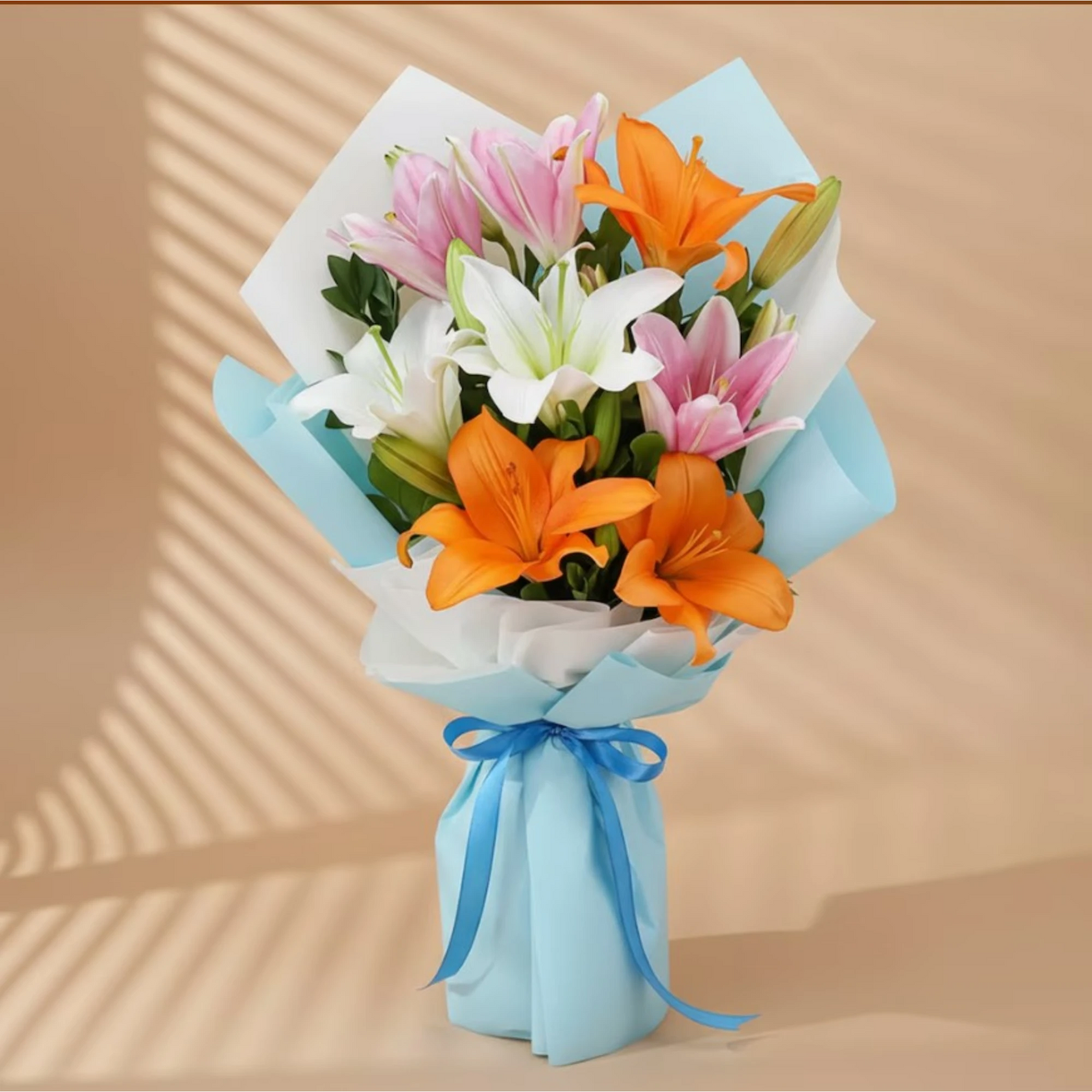 Bouquet of mixed Asiatic lilies with pink, white, and orange flowers wrapped in blue paper