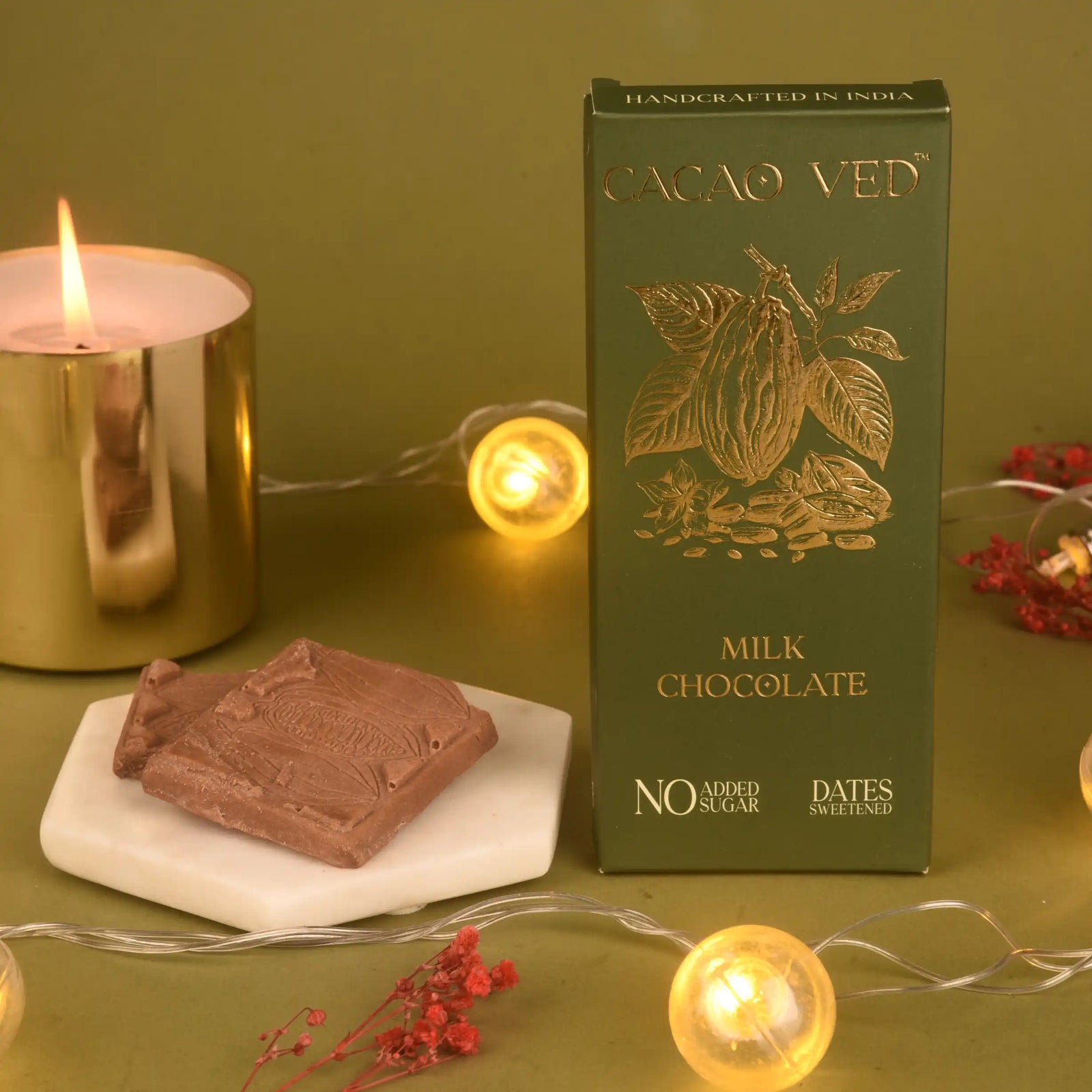 Milk Chocolate - Date-Sweetened | No Added Sugar, Guilt-Free bar by Cacao Ved with elegant green and gold packaging, placed beside a chocolate piece and festive lights.