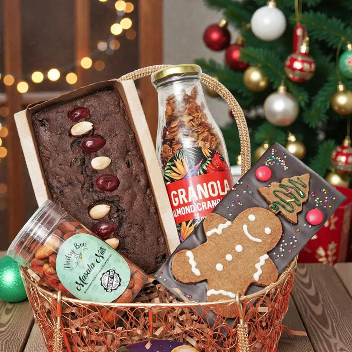Fusion of Flavors: Christmas Hamper Gift Set featuring plumcake, almond cranberry granola, masala nuts, and festive chocolate bar in a decorative basket.
