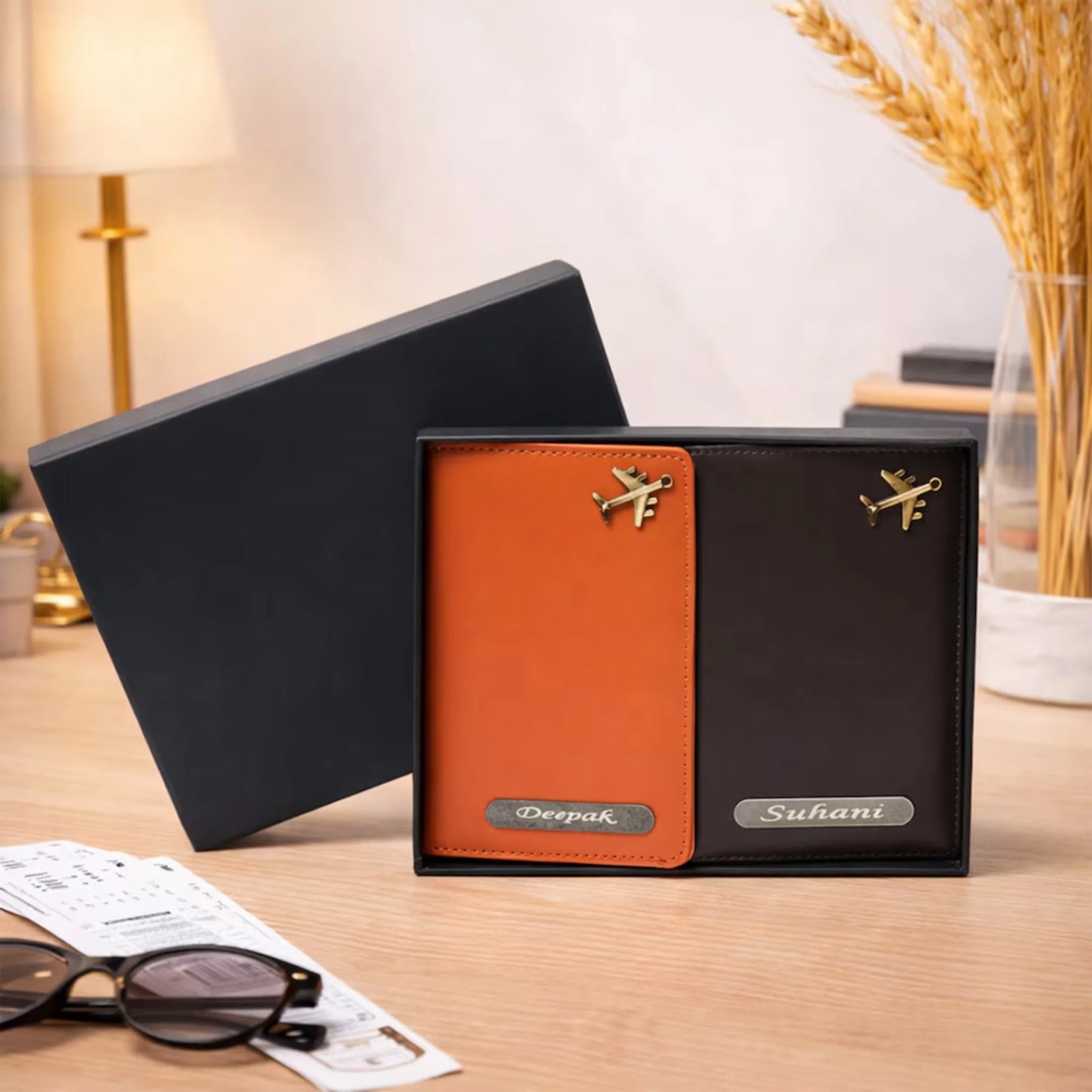 Two leather wallets, one orange and one black, with 'Deepak' and 'Suhani' branding, on a wooden surface.