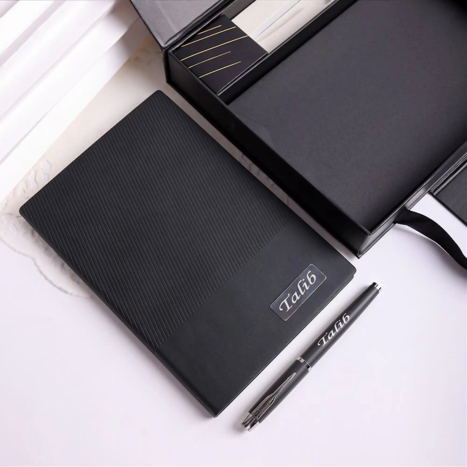 Black notebook and pen set with 'Talib' branding on a white surface